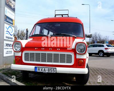 Alter alter FORD-WOHNWAGEN in Rot und Weiß. Frontalansicht. Rostiger Stahl-Lagerregal oben. Öffentlicher Parkplatz. Schilderpylon seitlich lagern. Stockfoto