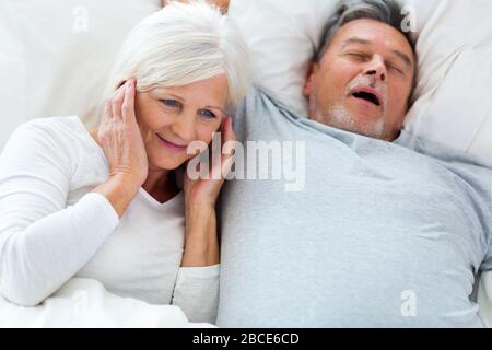 Der ältere Mann schnarcht und die Frau bedeckt Ohren Stockfoto