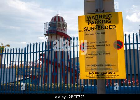 Southend-on-Sea, Großbritannien. April 2020. Ein gelbes Warnschild an der Western Esplanade, Southend-on-Sea, kündigt eine vorübergehende Aussetzung der Parken- und Entladebeschränkungen während der COVID-19-Pandemie an. Die Mitteilung gilt für Wochenenden und Feiertage zwischen dem 10. April und dem 26. April 2020 gemäß Abschnitt 14 Absatz 2 des RTRA 1984. Hinter dem Zaun ist der Hinterbau von Adventure Island zu sehen, was die Auswirkungen der Lockdown auf Freizeit und Tourismus deutlich macht. Penelope Barritt/Alamy Live News Stockfoto