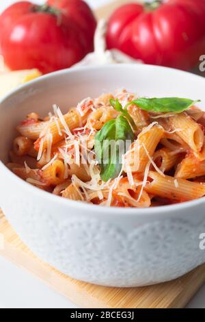 Klassische italienische Penne-Pasta arabiata mit Zutaten im Hintergrund: Frische Tomaten, Basilikum, Knoblauch und Parmesan Stockfoto