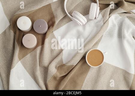 Flaches Lay aus drei kleinen aromatischen Kerzen, weißen Kopfhörern und einer Tasse frischen Cappuccino auf Leinen oder Baumwollpflaumen Stockfoto