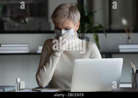 Betonte junge Geschäftsfrau in der medizinischen Maske und Schutzhandschuhe hustend. Stockfoto