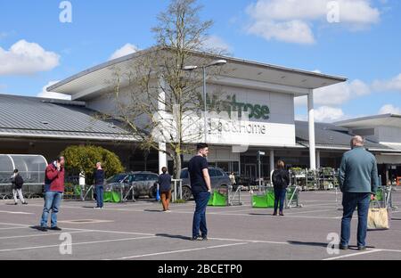 Menschen, die 2 Meter voneinander entfernt in einem Parkplatz stehen, warten auf einen Supermarkt, um während der Coronavirus Covid19-Pandemie Lebensmittel in Großbritannien zu kaufen Stockfoto