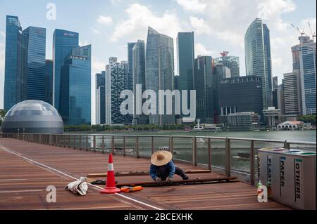 02.04.2020, Singapur, Republik Singapur, Asien - Arbeiter reparieren Holzbohlen entlang der Küste in Marina Bay mit der Skyline der Stadt des CBD. Stockfoto