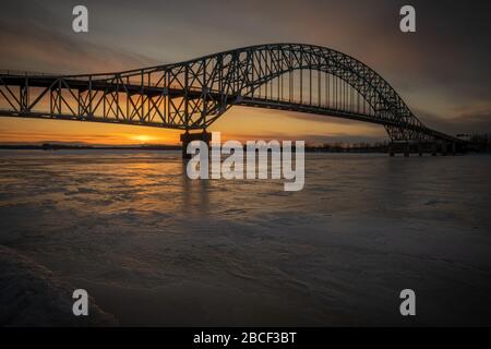 Burton Bridge außerhalb Fredericton, New Brunswick, Kanada bei Sonnenuntergang im Winter. Gefrorener Fluss. Stockfoto