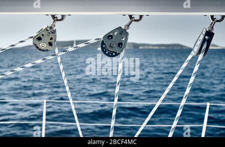 Nahaufnahme der segelschiffseile bei sonnigem Wetter, Riemenscheiben und Seile am Mast, Jachtsport, Schiffsausrüstung, Meer ist im Hintergrund Stockfoto