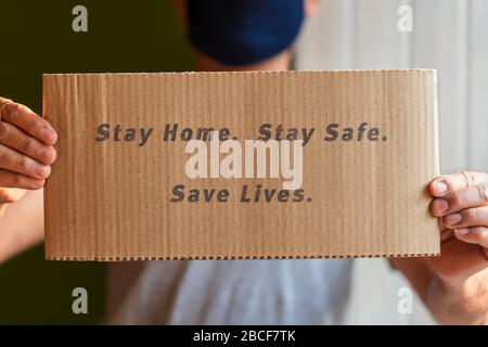 Coronavirus Konzept. Mann, der eine schützende medizinische Maske trägt und Poster zeigt, um zu Hause zu bleiben, bleibt sicher und unterstützt die soziale Distanzierungskampagne für diese pande Stockfoto