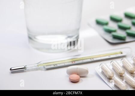 Pillenpackungen, Industitialthermometer mit bunten Medikamenten auf weißem Hintergrund, Tisch, Heilung, Impfstoff, Medikamente, erste Hilfe Stockfoto