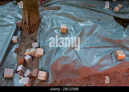 Kopfsteinpflaster wiegen ein Kunststoffblech ab, das eine Pflastersteinbaustelle bedeckt Stockfoto