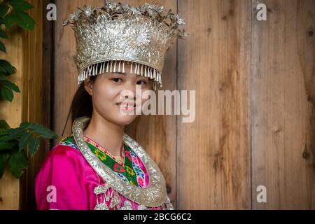 Feng Huang, China - August 2019: Schöne Chinesin in traditioneller Volkstracht gekleidet und posiert für ein Bild vor Holzhintergrund von Stockfoto