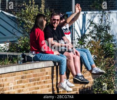 London, Großbritannien. April 2020. Ein sonniger Tag und Freunde mit Getränken klettern auf die Dachwand eines Nachbarhauses, um die letzten Sonnenstrahlen zu bekommen. Der "Lockdown" setzt sich für den Coronavirus (Covid 19)-Ausbruch in London fort. Credit: Guy Bell/Alamy Live News Stockfoto