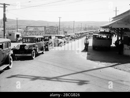 Eine lange Reihe von Autos warten auf die Zollabfertigung und überqueren die Grenze zwischen den Vereinigten Staaten und Mexiko in Tijuana, Mexiko und San Ysidro, Kalifornien, 1920er Jahre. Fotografie von Burton Holmes. Stockfoto