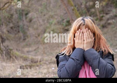 Mädchen weint in der Natur. Person in Qual hält die Hände auf seinem Gesicht. Depressive junge Frau im Hemd, die in der Natur von Wut und Traurigkeit ausgebrochen ist. Hände Stockfoto