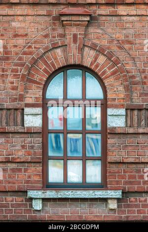 Fenster mit einem Bogen auf den Hintergrundwand aus braunem Backstein. Aus der Serie Fenster von Sankt-Petersburg. Stockfoto