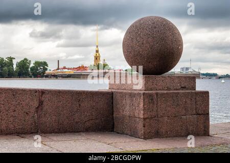 Zusammensetzung einer Kugel aus Granit auf einem Sockel aus Granit auf dem Pfeil der Insel Vasilievsky. Im Hintergrund ist die Festung Peter und Paul zu sehen. Stockfoto