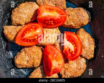 Ein Gericht aus gebratenem Fleisch mit roten Tomaten in einer Pfanne. Stockfoto
