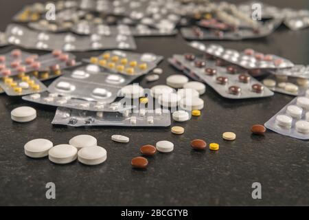 Verschiedene lose Tabletten und verpackte Medikamente liegen auf einem schwarzen Tisch. Stockfoto