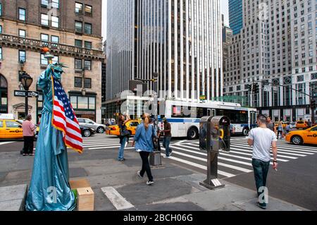 Eine in Freiheitsstatue gekleidete Menschenstatue mit Touristen, die darauf warten, am Ausgang des Central Park plaza mit Blick auf die Grand Army Plaz fotografiert zu werden Stockfoto