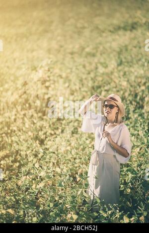 Junge Frau im grünen Feld in weißem Kleid und mit Hut und Sonnenbrille Stockfoto
