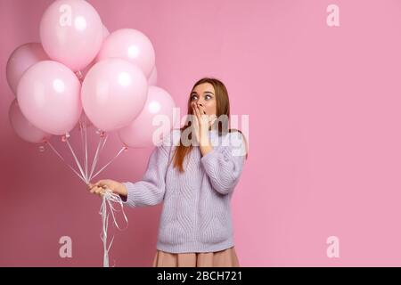 Überraschte kaukasische Mädchen posieren mit pastellrosa Luftballons isoliert über rosafarbenem Hintergrund. Schöne fröhliche junge Frau in einem Geburtstagsurlaub, Platz für Text Stockfoto