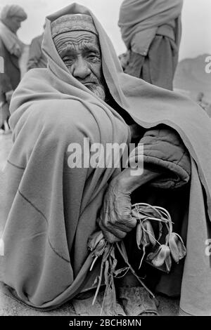 Ein älterer afghanischer Mann hält einen Haufen verblichener Tulpen, als er auf dem Friedhof seines Sohnes trauert, der im Bürgerkrieg von afghanischen Mudschaheddin nach der Beerdigung auf dem Martyrs Hill Burial Grounds am 27. April 1989 in Kabul, Afghanistan, getötet wurde. Stockfoto