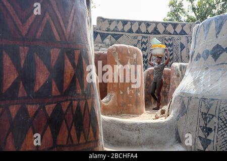 Afrika, Burkina Faso, Region Pô, Tiebele. Stadtansicht des königlichen Hofdorfes in Tiebele. Eine Frau geht mit einem Becken Stockfoto