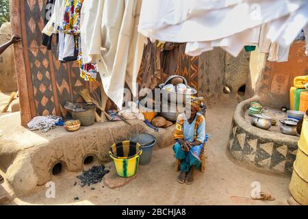Afrika, Burkina Faso, Region Pô, Tiebele. Stadtansicht des königlichen Hofdorfes in Tiebele. Eine Frau sitzt unter einer hangigen Wäsche Stockfoto