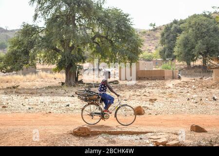 Afrika, Burkina Faso, Region Pô, Tiebele. Ein Mann fährt auf einer unbefestigten Straße mit einem Fahrrad an seinem Fahrrad Stockfoto