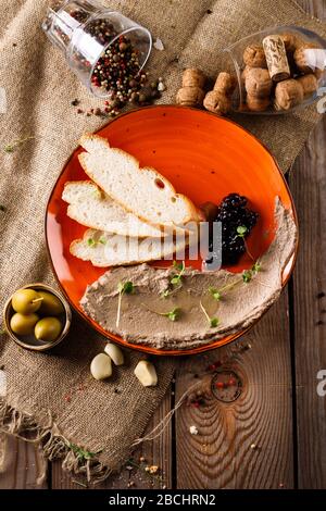 Frische Pate auf einem Teller, neben Brotscheiben, gegen einen Holztisch geschmiert Stockfoto