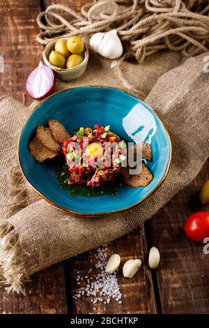 Beef Tatar mit eingepickter Gurke in blauer Platte auf dem Grund des Burlap Stockfoto