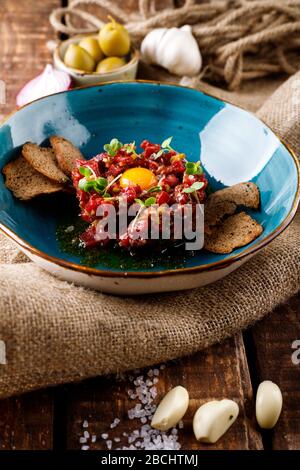 Beef Tatar mit eingepickter Gurke in blauer Platte auf dem Grund des Burlap Stockfoto