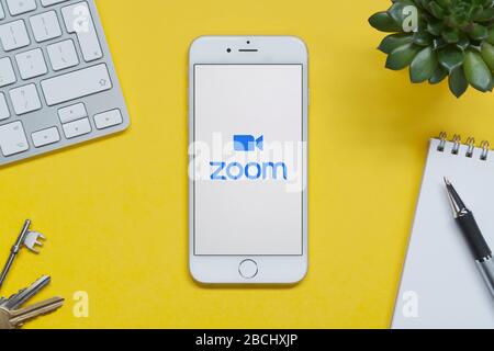 Ein iPhone mit Zoom-Logo liegt auf einem gelben Hintergrund Tisch mit Tastatur, Tasten, Notizblock und Pflanze (nur für redaktionelle Verwendung). Stockfoto