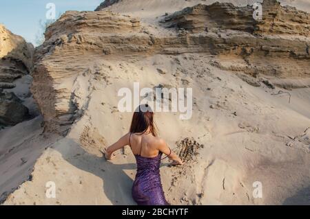 Braunhaarige Frau im violett glitzernden Kleid liegt am Sandhang Stockfoto