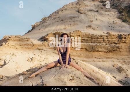 Braunhaarige Frau in violett glitzerndem Kleid, die auf Sandhang sitzt Stockfoto