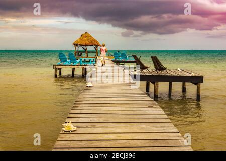 Caye Caulker, Belize - 20. Dezember 2016: Frau, die auf einer Anlegestelle aus Holzsteg spaziert und den malerischen, entspannenden Blick auf das Meer auf Caye Caulker Belize Caribbean hat. Stockfoto