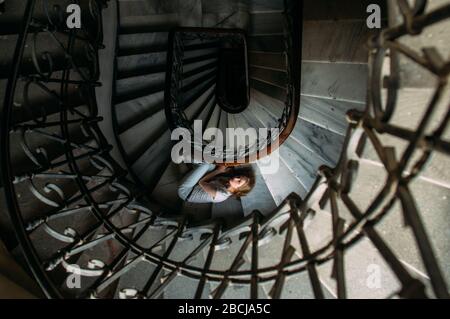 Schönes Mädchen mit blonden Haaren liegt auf einer Wendeltreppe im alten Haus Stockfoto