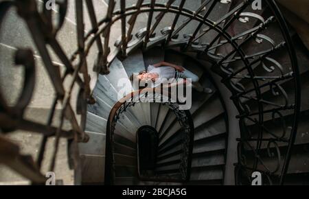 Schönes Mädchen mit blonden Haaren liegt auf einer Wendeltreppe im alten Haus Stockfoto