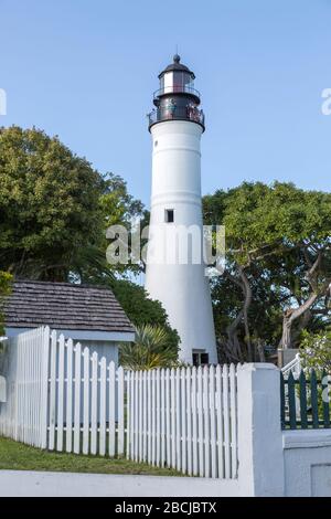 Key West Lighthouse, umgeben von einem weißen Zaun und Bäumen, am sonnigen, blauen Himmelstag. Touristen, die den Blick von oben nehmen. Florida, USA. Stockfoto