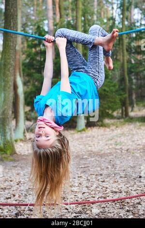 Kleines Mädchen, das auf dem Seil auf dem Spielplatz im Park umgedreht hängt Stockfoto