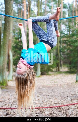 Kleines Mädchen, das auf dem Seil auf dem Spielplatz im Park umgedreht hängt Stockfoto