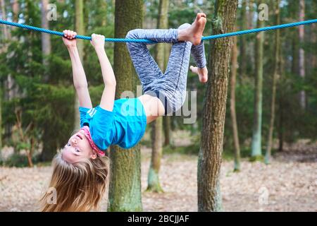 Kleines Mädchen, das auf dem Seil auf dem Spielplatz im Park umgedreht hängt Stockfoto