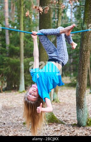 Kleines Mädchen, das auf dem Seil auf dem Spielplatz im Park umgedreht hängt Stockfoto