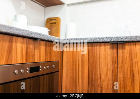 Die moderne, braun-orangefarbene Holzküche verfügt über Schränke mit Mikrowelle auf der Unterseite und Knöpfe an der Arbeitsplatten in der Hauswohnung Stockfoto