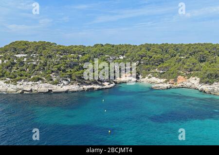 Landschaft mit türkisfarbenem Wasser, Klippen und üppig grüner Vegetation mit blauem Himmel und hellen Wolken in Menorca, Spanien. Stockfoto