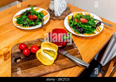 Häckseln von Gemüse über dem Blick auf den Schneidtisch mit zwei Platten frischen veganen Salats mit rot gelben Paprika und Tomaten Stockfoto