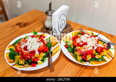 Zwei Teller veganer Salat mit rotgelben Paprika, Zwiebeln und Tomaten auf dem Tisch mit Gabel, Salzschüttler und Serviette Stockfoto