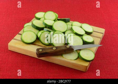 In Scheiben geschnittener frischer Rohzucchini-Squash auf Holzschneidebrett mit Messer Stockfoto