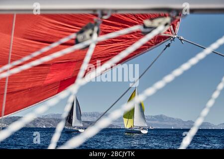 Segelboote nehmen bei Sonnenuntergang an einer Segelregatta Teil, sehen durch die Seile, Rennen von Segelbooten, Spiegelung der Segel auf dem Wasser, bunte Spinnaker, Insel Stockfoto