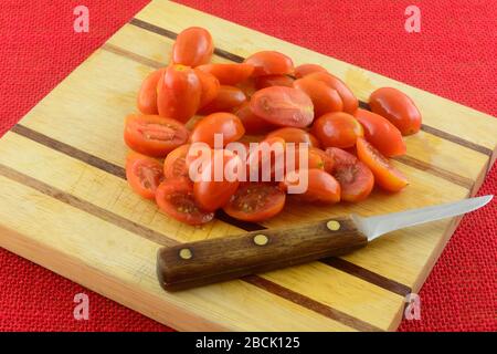 In Scheiben geschnittene frische, rohe Traubentomaten auf Holzschneidebrett mit Messer Stockfoto