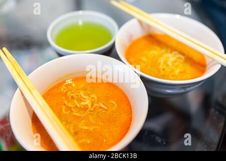 Makro-Nahaufnahme von zwei würzigen roten Ramen Nudelsuppen-Schüsseln mit Essstäbchen japanische asiatische Mahlzeit und grünem Tee Stockfoto